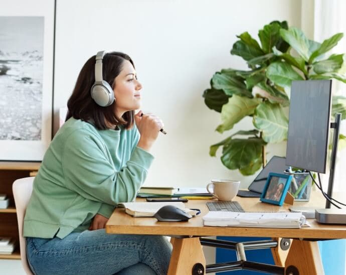 Mujer con auriculares que sostiene un bolígrafo y mira al monitor de un PC