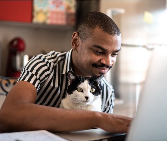 Hombre que utiliza un ordenador portátil mientras sostiene un gato