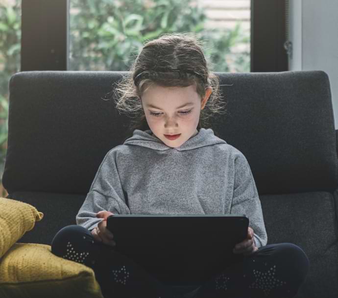 Chica en un sofá que utiliza un ordenador portátil e inicia Norton Family