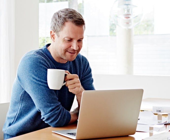 Hombre en su casa que utiliza el ordenador portátil mientras bebe café