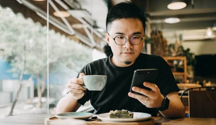 Hombre bebiendo café mientras mira el teléfono móvil e inicia Norton 360 Estándar.