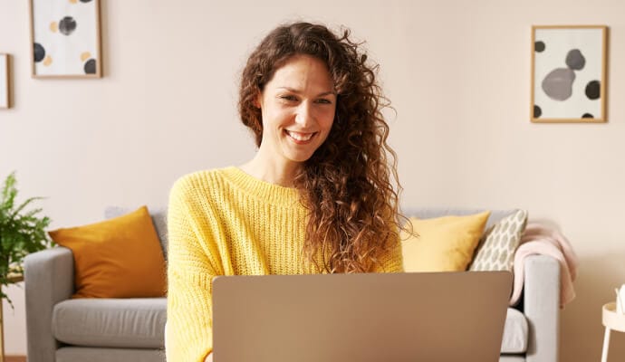 Mujer que sonríe y utiliza un portátil en el que inicia Norton Safe Search